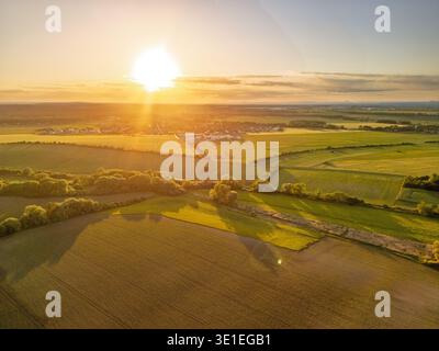 Il sole sorge sopra i campi agricoli pianeggianti illuminando i terreni coltivati. Sono visibili lunghe ombre di alberi e siepi. Foto Stock