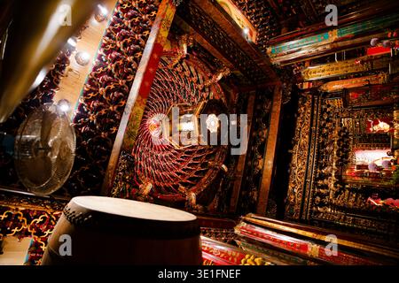Primo piano del soffitto decorato nel Tempio di Longshan, con intricate incisioni rosse e oro, lanterne radianti e una calda illuminazione ambientale. Foto Stock
