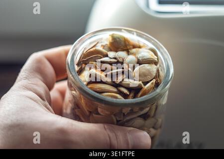nella mano dell'uomo c'è un barattolo di semi di zucca con i resti di una zucca sopra di loro. conservazione e asciugatura naturali non in fabbrica. Foto di alta qualità Foto Stock