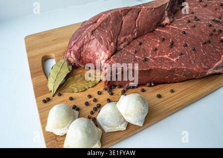 Un pezzo di carne di manzo e gnocchi di manzo su un tavolo da cucina. Uno striscione con prodotti a base di carne marmorizzati di manzo grani di pepe e foglie di alloro. Foto di alta qualità Foto Stock