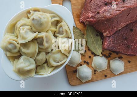 Un pezzo di carne di manzo e gnocchi di manzo su un tavolo da cucina. Uno striscione con prodotti a base di carne marmorizzati di manzo grani di pepe e foglie di alloro. Foto di alta qualità Foto Stock