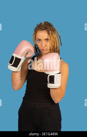 Giovane donna con dreadlock che indossa guanti da boxe rosa in posa da combattimento Foto Stock