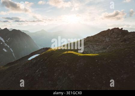Veduta aerea di una figura solitaria che si staglia sulla luce dorata su una cresta erbosa di montagna, con uno sfondo di cime nebbiose, Obergoms e Wall Foto Stock
