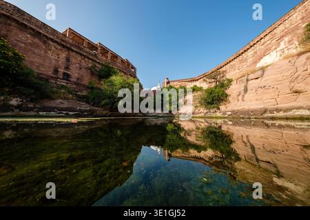Un'ampia vista del tempio Chamunda Mataji riflessa in uno stagno di muschio all'interno delle mura di arenaria rossa del forte Mehrangarh a Jodhpur. Foto Stock