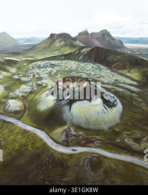Vista aerea di un paesaggio vulcanico con campi di lava ricoperti di muschio e una strada tortuosa che conduce a una montagna a forma di cono, Rangárþing ytra, Islanda. Foto Stock