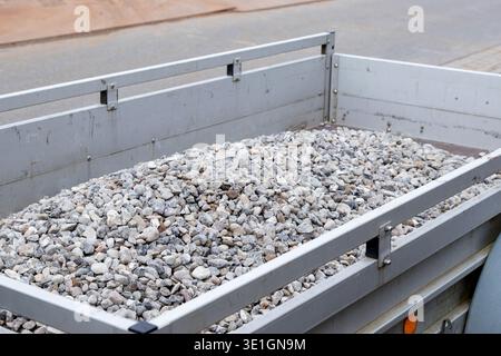 Rimorchio riempito con piccole pietre di ghiaia parcheggiate in un cantiere, che mostra una vista ravvicinata della struttura di ghiaia e della struttura metallica del rimorchio Foto Stock