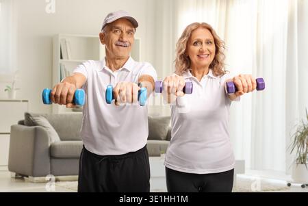 Uomo e donna sorridenti maturi che si esercitano con i manubri a casa in salotto Foto Stock