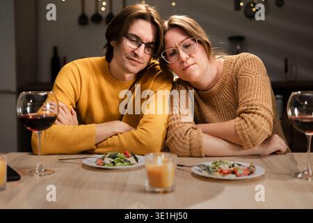 Una coppia stanca bruciata e innamorata seduta testa a testa a tavola e cena a casa la sera. Copia spazio Foto Stock
