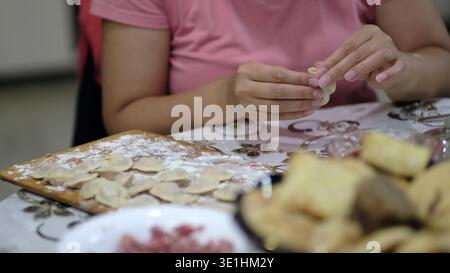 Primo piano di mani che modellano piccoli gnocchi su un tavolo da cucina infarinati, catturati da un angolo laterale con una luce soffusa per interni. La casa tranquilla Foto Stock
