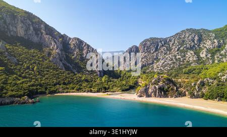 Splendida vista aerea di una spiaggia di sabbia isolata accoccolata tra spettacolari scogliere calcaree coperte da lussureggiante vegetazione verde. Olimpos, Kemer, Antalya Foto Stock