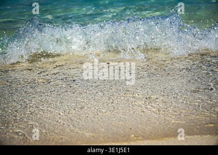Onde oceaniche che si infrangono dolcemente sulla costa sabbiosa della spiaggia in acque poco profonde e cristalline, vista ravvicinata. Foto Stock