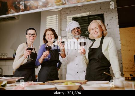 Diversi adulti di mezza età e chef che partecipano alla lezione di cucina per tostare il vino Foto Stock