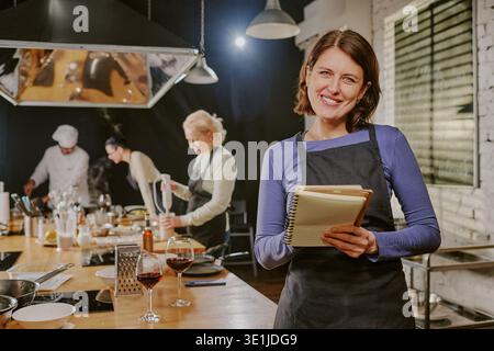 Donna caucasica di mezza età che conduce una lezione di cucina e sorride alla camera Foto Stock