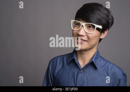 Studio shot del giovane uomo asiatico indossando occhiali cerca smart contro uno sfondo grigio Foto Stock