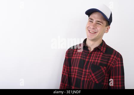 Studio shot del giovane uomo bello indossare berretto da baseball rosso e camicia a scacchi contro uno sfondo bianco Foto Stock