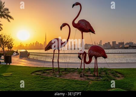 Vista del tramonto dal Dubai Creek Harbour verso lo skyline con la famosa statua del fenicottero di fronte Foto Stock