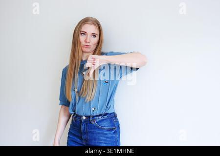 Giovane donna che mostra un gesto con il pollice in basso su sfondo neutrale che esprime rifiuto antipatico o concetto di opinione negativa Foto Stock