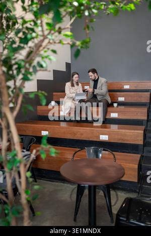 Partner commerciali che discutono idee e rivedono le attività sui posti a sedere in legno sotto foglie verdi. Idee, compiti, foglie verdi, discussioni, affari. Foto Stock