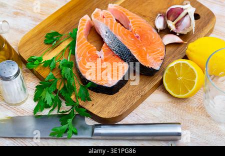 Bistecche di salmone crudo su tagliere di legno con verdure, limone e aglio Foto Stock