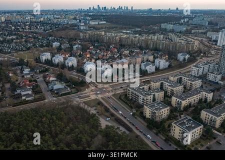 Vista aerea al crepuscolo di un sobborgo di Varsavia con bassi blocchi, case, e un incrocio a più corsie, bosco di fronte, skyline distante e Palazzo di culto Foto Stock