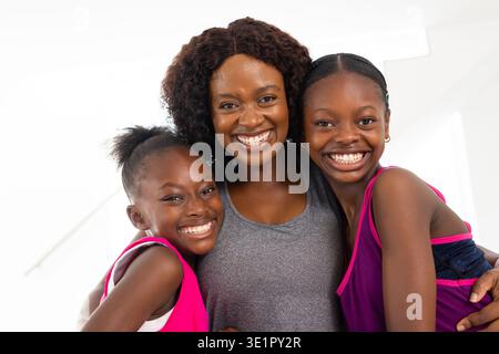 Madre afroamericana con ragazze sorridenti, appoggiate in un luminoso studio indossando canotte e canotte sportive Foto Stock