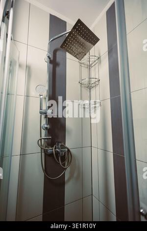 L'acqua scorre dalla doccia in un bagno con piastrelle. Lo spazio ha un ripiano per il sapone e altri oggetti. La luce intensa penetra nell'area dall'alto. Foto Stock