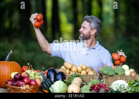 Agricoltore che raccoglie verdure fresche nell'orto rurale. Uomo degli anni '40 che controlla zucche, carote, mais, broccoli, peperoni, pomodori e patate. Agronomo Foto Stock