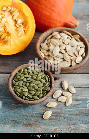 Zucche fresche e semi di zucca sbucciati e non sbucciati in ciotole di legno su un tavolo di legno, primo piano Foto Stock