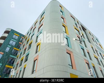 Un alto edificio sorge in un ambiente urbano caratterizzato da pannelli colorati in varie sfumature all'esterno. Il cielo è grigio e l'edificio appare solo Foto Stock