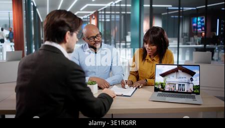 Giovane coppia che firma Un contratto con l'agente immobiliare mentre il consulente finanziario guarda. Foto Stock