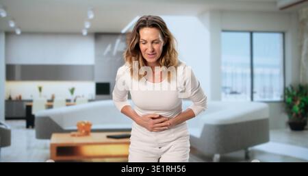 Donna di mezza età che soffre di mal di stomaco nel salotto di casa Foto Stock