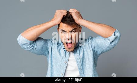 Frustrati Guy tirando i suoi capelli fuori su grigio di sfondo per studio Foto Stock