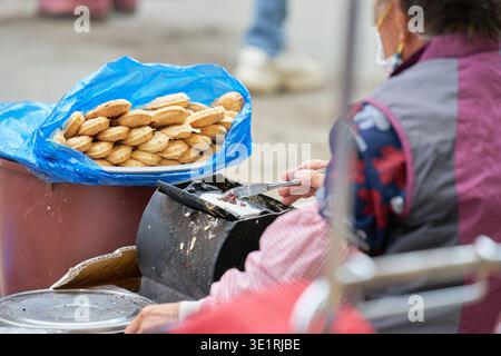 Un venditore versa pastella per preparare Bungeoppang, riempiendo un sacchetto blu con i caldi dolci a forma di pesce, catturando la confortevole essenza della strada coreana Foto Stock