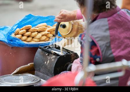 Un venditore versa pastella per preparare Bungeoppang, riempiendo un sacchetto blu con i caldi dolci a forma di pesce, catturando la confortevole essenza della strada coreana Foto Stock