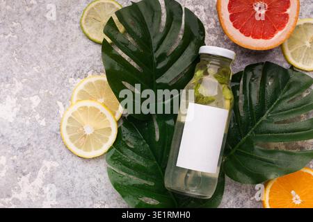 Foglie di Monstera e bottiglia d'acqua tropicale su sfondo grigio. Foto Stock