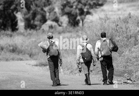 Johannesburg, Sudafrica - lavoratori migranti disoccupati non identificati camminano su una strada sterrata fuori città in cerca di un prossimo lavoro Foto Stock