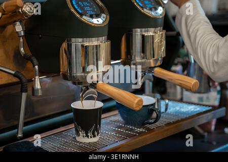 Macchina espresso che distribuisce il caffè in due tazze, una nera e una blu, con la mano del barista visibile in un bar Foto Stock