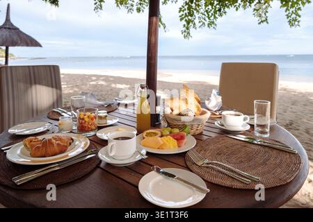 Concediti un delizioso pasto mattutino su una tranquilla spiaggia di Mauritius. Con frutta vibrante, dolci caldi e splendide viste sull'oceano, questa esperienza cattura l'essenza del viaggio di lusso. Foto Stock