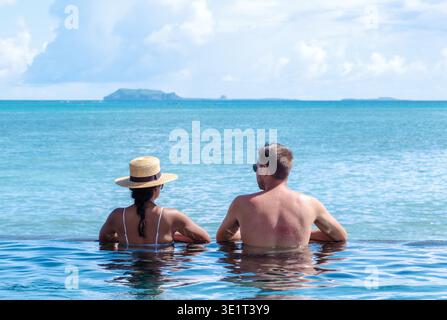 Due persone godono di un momento sereno al bordo di una splendida piscina a sfioro che si affaccia sull'oceano turchese mozzafiato di Mauritius. Foto Stock