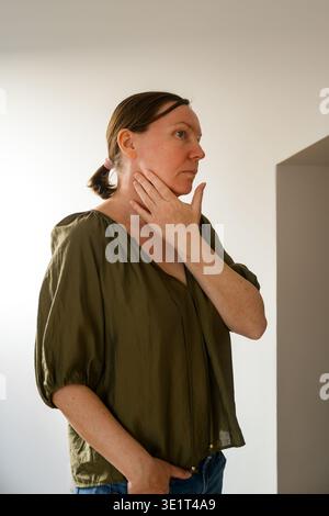 Donna premurosa che tocca il collo nel profilo, ritratto minimalista degli interni, messa a fuoco selettiva Foto Stock
