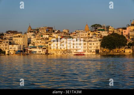 Il lungomare di Udaipur viene catturato al tramonto, mostrando la guglia del Tempio Jagdish che si innalza sopra gli edifici bianchi densamente pieni e il lago. Foto Stock