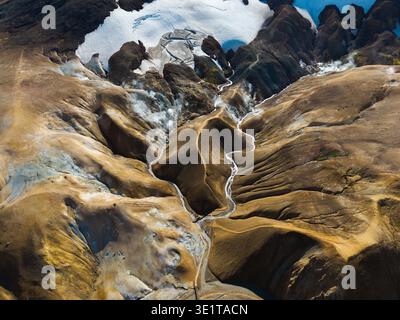 Vista aerea di aspre montagne dalla trama fitta che incontrano il ghiaccio glaciale, con tortuosi fiumi che si intagliano attraverso il paesaggio, creando un incredibile contrasto di terra Foto Stock