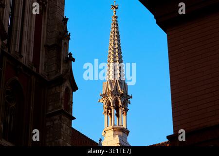 Intricate incisioni in pietra adornano l'alta guglia di una chiesa storica, sagomata contro il vibrante cielo serale Foto Stock