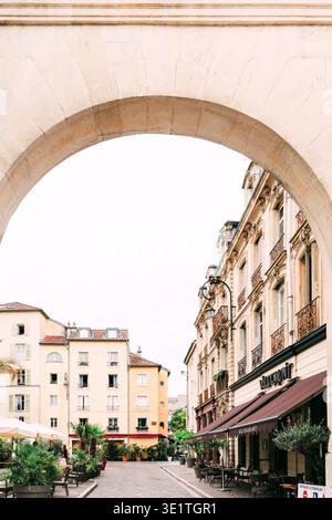 Ammira attraverso un grande arco di pietra una strada di Nancy, in Francia, con edifici ornati, terrazze e alberi Foto Stock