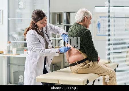 Dottoressa donna che esamina la parte posteriore dell'uomo anziano in clinica Foto Stock