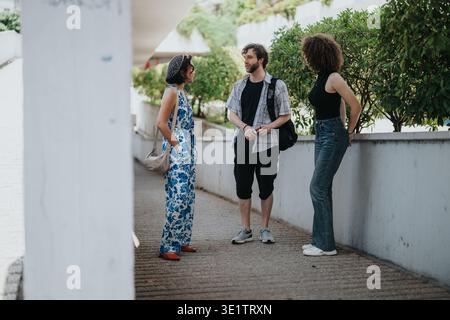 Tre amici chiacchierano su un marciapiede urbano soleggiato, abiti casual e verde sullo sfondo Foto Stock