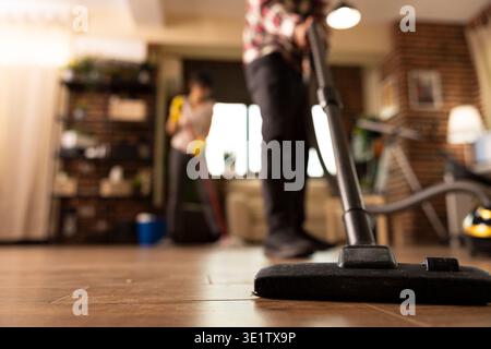 Primo piano ritagliato di un uomo che aspira in soggiorno durante la pulizia del fine settimana a casa. Appartamento individuale maschile in ordine, mantenendo la pulizia e completando le faccende domestiche quotidiane. Foto Stock