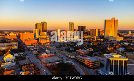 Vista aerea dei grattacieli che perforano l'orizzonte mentre il sole tramonta proietta un bagliore dorato sul paesaggio urbano di Fort Worth, Texas, Stati Uniti. Foto Stock