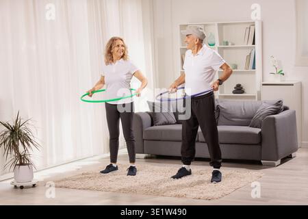 Felice coppia matura che si esercita con hula hoops a casa Foto Stock