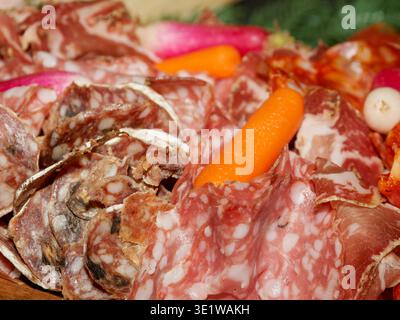 Primo piano di un assortimento di salumi con salumi a fette e affettati con piccole verdure. Vassoio di antipasti gourmet in un ambiente rustico Foto Stock